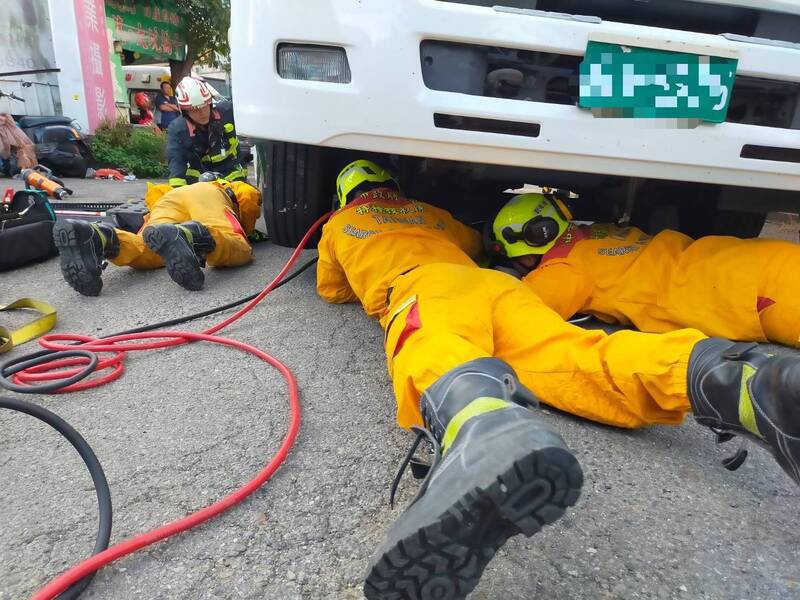 古女骑机车载朋友罗女，2人都被卷进大货车底，消防人员设法法营救。（图由民众提供）