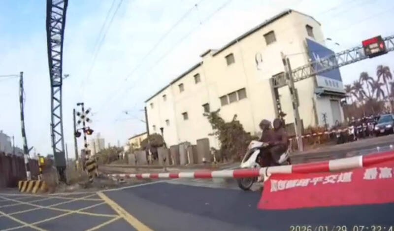 双载的机车行经永康乌水桥平交道时，遮断器已完全放下，骑士仍闯过平交道。（读者提供）